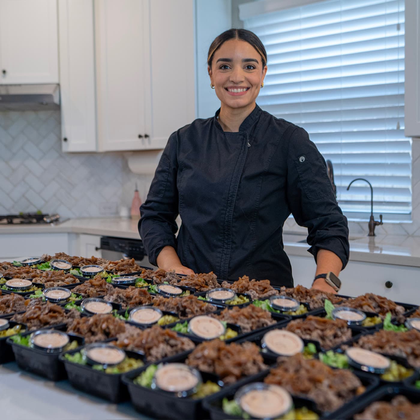 Chef Pamela in her kitchen, behind a counter full of the week's prepped bowls.